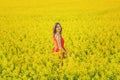 Young beautiful girl in a red dress close up in the middle of the yellow field with the radish flowers closeup Royalty Free Stock Photo