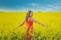 Young beautiful girl in a red dress close up in the middle of the yellow field with the radish flowers closeup