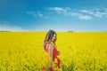 Young beautiful girl in a red dress close up in the middle of the yellow field with the radish flowers closeup Royalty Free Stock Photo