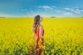 Young beautiful girl in a red dress close up in the middle of the yellow field with the radish flowers closeup Royalty Free Stock Photo