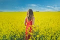 Young beautiful girl in a red dress close up in the middle of the yellow field with the radish flowers closeup Royalty Free Stock Photo