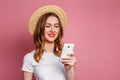 Young beautiful girl with red lipstick in a straw hat and white T-shirt smiles and holds a mobile phone in her hands. Woman is Royalty Free Stock Photo