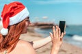 Young beautiful girl in a red santa claus hat and swimsuit makes a selfie on the seashore Royalty Free Stock Photo