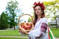 young beautiful girl in red wreath of flowers on her head red poppies in vyshyvanka red apples take an apple with hands Royalty Free Stock Photo