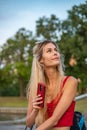 A young beautiful girl sits on a bench and smiles, holds a phone in her hands and looks into the sky Royalty Free Stock Photo