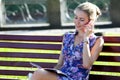 Young beautiful girl sitting on a bench looks magazine and speaks on a mobile phone Royalty Free Stock Photo