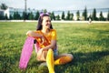 Young beautiful girl sitting on a lawn holding a skateboard in her hand in a yellow T-shirt and yellow socks in the open Royalty Free Stock Photo