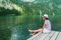 Young beautiful girl sitting on a pier by Konigssee lake with clear green water