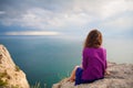 Beautiful girl sitting on rock and looking at sea