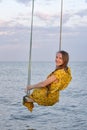 Young beautiful girl sitting on a rope swing on sea background. Vertical frame Royalty Free Stock Photo