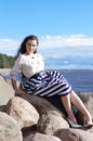 Young beautiful girl sitting on the stone resting shore