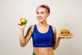 A young beautiful girl smiles and holds hamburger and green apple on a light background. Conception healthy eating and fast Royalty Free Stock Photo