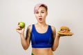 A young beautiful girl smiles and holds hamburger and green apple on a light background. Conception healthy eating and fast Royalty Free Stock Photo