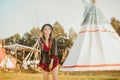 Young beautiful girl smiling on background teepee, tipi- native indian house. Pretty girl in hat with long cerly hair, in dress Royalty Free Stock Photo