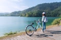 Young beautiful girl stand near a bicycle to looking at the view on bike trail at the lake in the morning. Active people. Outdoors