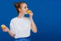 A young beautiful girl standing on a blue background holding lemons in her hand and biting Royalty Free Stock Photo