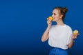 A young beautiful girl standing on a blue background holding lemons in her hand and biting Royalty Free Stock Photo