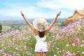 Young and beautiful girl standing and raising her arms in the midst of cosmos flowers filed and put cell phone in the back pocket Royalty Free Stock Photo