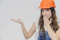 A young beautiful girl stands on a gray background. It is dressed in an orange helmet on the head. Royalty Free Stock Photo