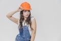 A young beautiful girl stands on a gray background. It is dressed in an orange helmet on the head. During this, he looks Royalty Free Stock Photo