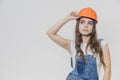 A young beautiful girl stands on a gray background. It is dressed in an orange helmet on the head. During this, he looks Royalty Free Stock Photo