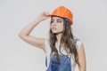 A young beautiful girl stands on a gray background. It is dressed in an orange helmet on the head. During this, he looks Royalty Free Stock Photo