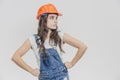 A young beautiful girl stands on a gray background. It is dressed in an orange helmet on the head. Royalty Free Stock Photo
