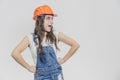 A young beautiful girl stands on a gray background. It is dressed in an orange helmet on the head. Royalty Free Stock Photo