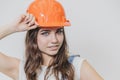 A young beautiful girl stands on a gray background. It is dressed in an orange helmet on the head. During this time he Royalty Free Stock Photo