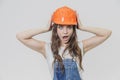 A young beautiful girl stands on a gray background. It is dressed in an orange helmet on the head. During this time he Royalty Free Stock Photo