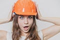 A young beautiful girl stands on a gray background. It is dressed in an orange helmet on the head. During this time he Royalty Free Stock Photo