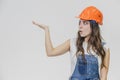 A young beautiful girl stands on a gray background. It is dressed in an orange helmet on the head. During this, he has a Royalty Free Stock Photo