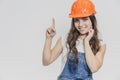 A young beautiful girl stands on a gray background. It is dressed in an orange helmet on the head. During this, he looks Royalty Free Stock Photo