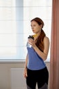 A young beautiful girl stands at the window with a shaker in her hands. sports food.