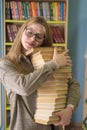 Young beautiful girl student holds in her hands a large stack of books in the library against the background of bookshelves Royalty Free Stock Photo