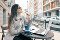 Young beautiful girl student wearing glasses warm coat sitting in an outdoor cafe with laptop computer cup of hot drink holding Royalty Free Stock Photo