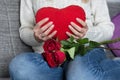 Female holding big red heart pillow in hand on her chest and sitting on bed and roses on knees Royalty Free Stock Photo