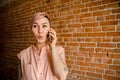 Young beautiful girl is talking on the mobile phone on a brick wall background Royalty Free Stock Photo