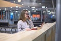 Young, beautiful girl talking on the phone standing at a table with a laptop and a cup of coffee at the airport