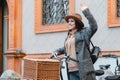 Young beautiful girl tourist is standing near a bicycle with a wicker basket and raising her hand calling someone