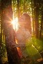 Young beautiful girl walking in forest and sun looking as star shining through the tree trunks. Model posing in the park in a Royalty Free Stock Photo