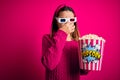 Young beautiful girl watching movie using 3d glasses eating box with popcorns smelling something stinky and disgusting,