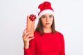 Young beautiful girl wearing Christmas Santa hat holding gift over isolated white background with a confident expression on smart Royalty Free Stock Photo