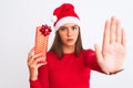 Young beautiful girl wearing Christmas Santa hat holding gift over isolated white background with open hand doing stop sign with Royalty Free Stock Photo