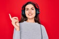 Young beautiful girl wearing modern headphones listening to music over red background with a big smile on face, pointing with hand Royalty Free Stock Photo