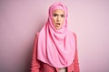 Young beautiful girl wearing muslim hijab standing over isolated pink background In shock face, looking skeptical and sarcastic,