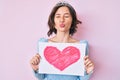 Young beautiful girl wearing princess crown holding heart draw looking at the camera blowing a kiss being lovely and sexy