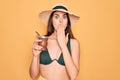 Young beautiful girl wearing swimwear bikini and summer hat drinking traditional mate drink cover mouth with hand shocked with