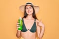 Young beautiful girl wearing swimwear bikini and summer hat holding alove vera sun protection with surprise face pointing finger