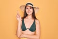 Young beautiful girl wearing swimwear bikini and summer sun hat over yellow background with a big smile on face, pointing with Royalty Free Stock Photo